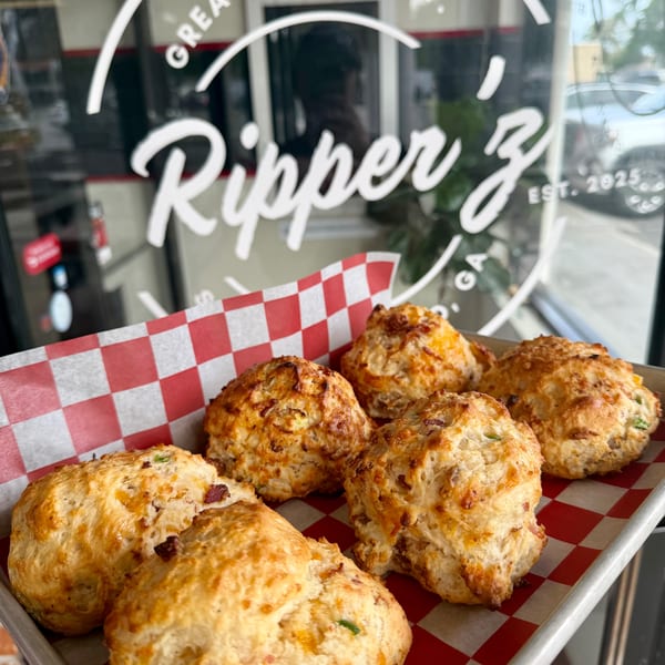 Savory biscuits with cheese and bacon on a tray with red and white checkered paper, in front of a window with "Ripper Z" logo.