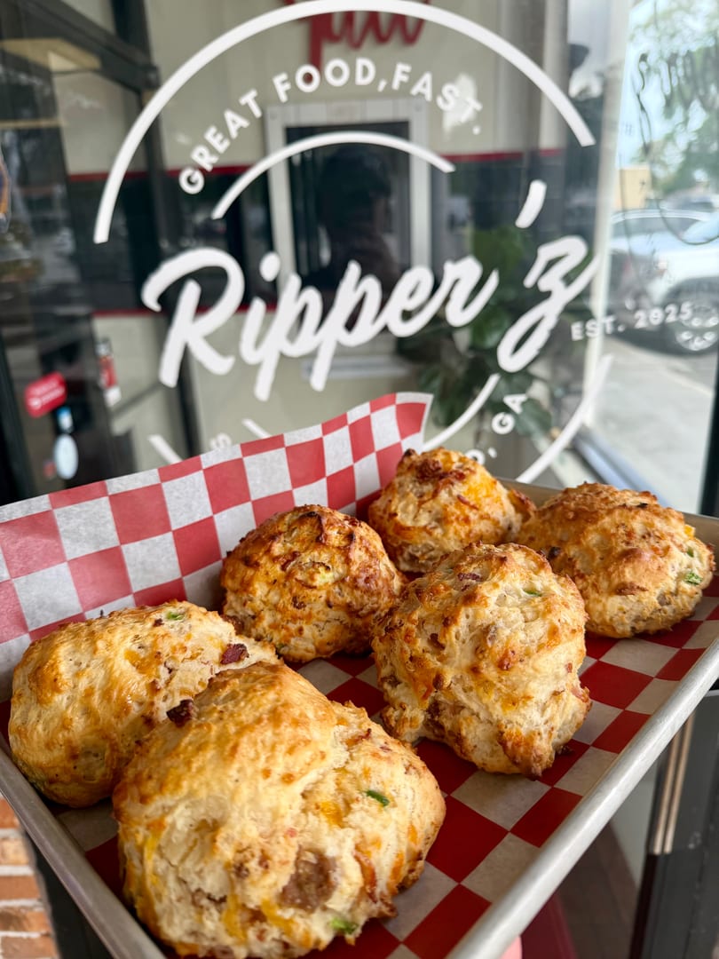 Savory biscuits with cheese and bacon on a tray with red and white checkered paper, in front of a window with "Ripper Z" logo.