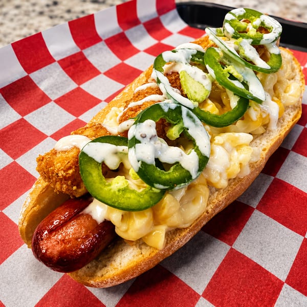 Hot dog in a bun with mac and cheese, fried chicken, jalapeños, and white sauce.